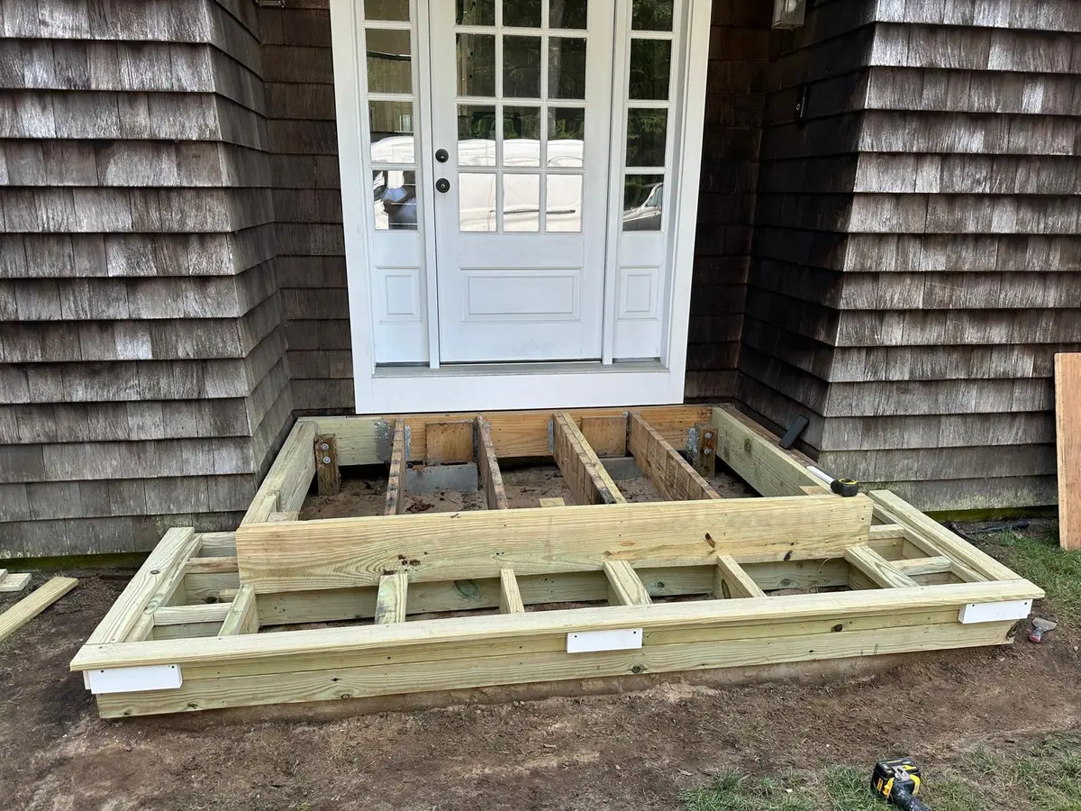 Deck framing in progress next to a cedar shake home